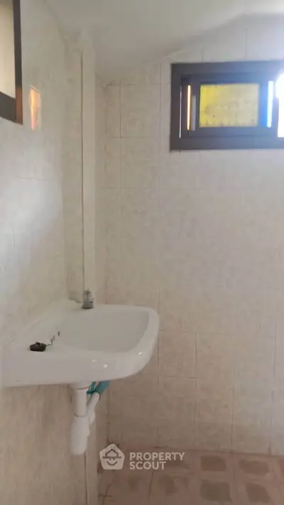 Compact bathroom with wall-mounted sink and small window, ideal for efficient space utilization.