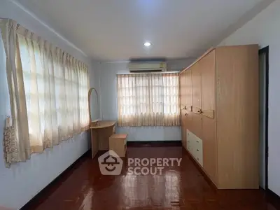 Spacious bedroom with wooden flooring and ample natural light, featuring built-in wardrobe and air conditioning.