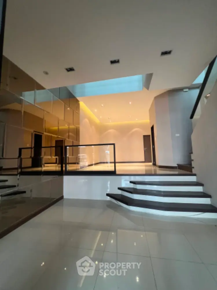 Luxurious open-plan living space with high ceilings, modern staircase, and sleek glass balustrades, perfect for upscale urban living.