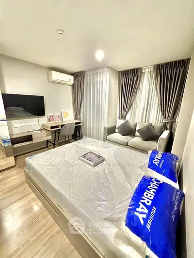 Modern bedroom with cozy sofa, wall-mounted TV, and stylish decor in a well-lit apartment.