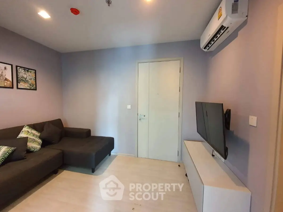 Modern living room with sleek design, featuring a comfortable sofa, wall-mounted TV, and air conditioning.
