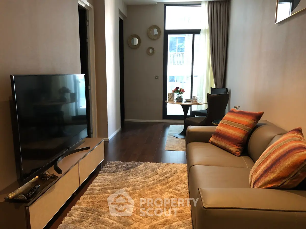 Modern living room with cozy sofa, stylish decor, and large TV, leading to a bright balcony view.
