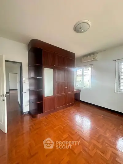 Spacious bedroom with wooden flooring and built-in wardrobe, featuring natural light and air conditioning.