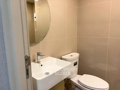 Modern bathroom with sleek fixtures and neutral tiles, featuring a round mirror and compact sink.