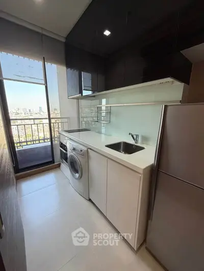 Modern kitchen with sleek cabinets, washing machine, and balcony view in urban apartment.