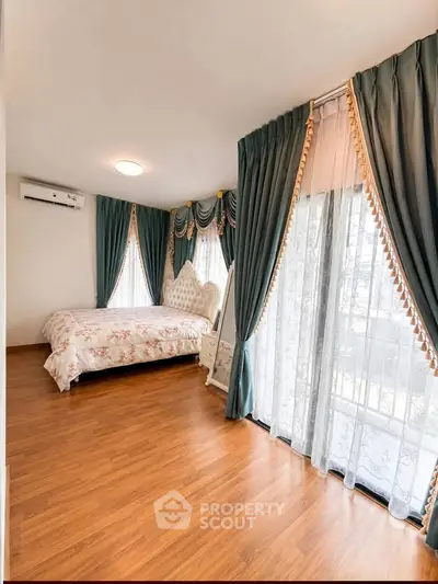 Spacious bedroom with elegant curtains and wooden flooring, featuring a cozy bed and ample natural light.