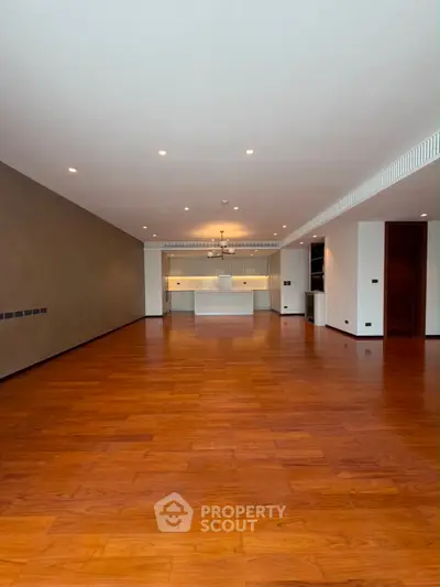 Spacious open-plan living room with wooden flooring and modern kitchen area.
