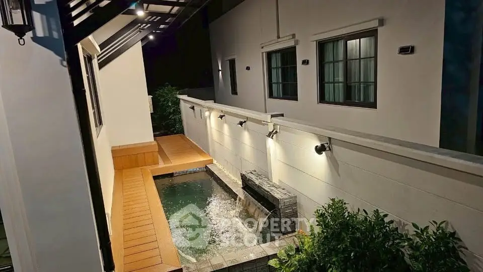 Charming night view of a modern home's exterior with a serene water feature and ambient lighting.