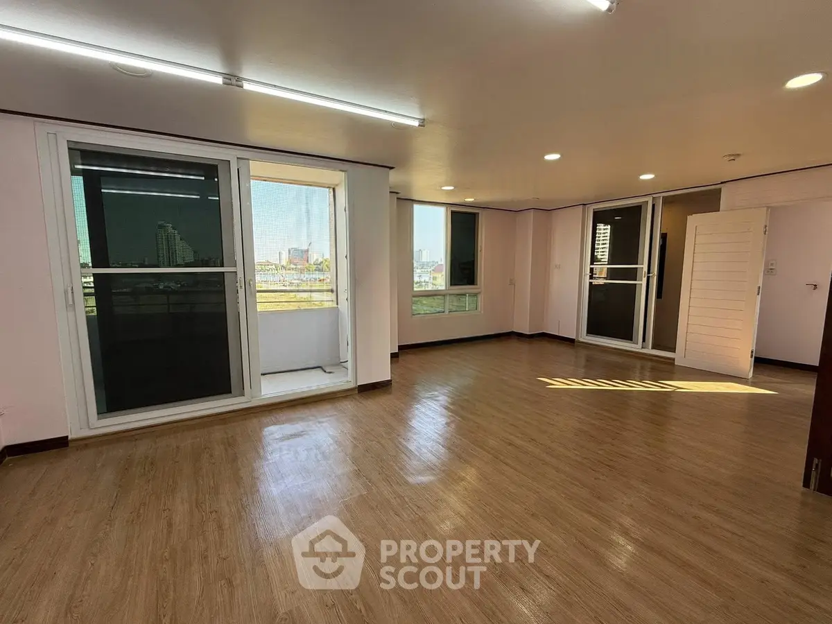 Spacious living room with large windows and balcony access, featuring modern flooring and ample natural light.