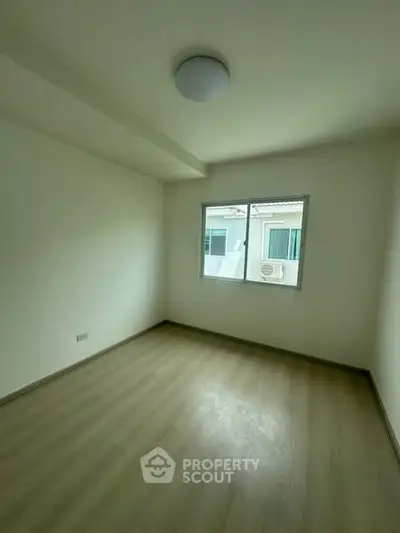 Spacious empty room with wooden flooring and large window offering natural light.