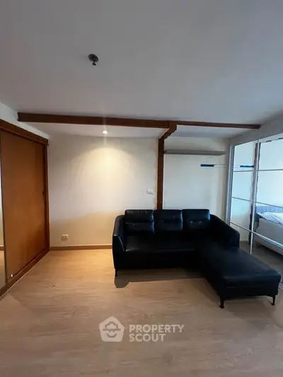 Spacious living room with modern black leather sofa and wooden flooring