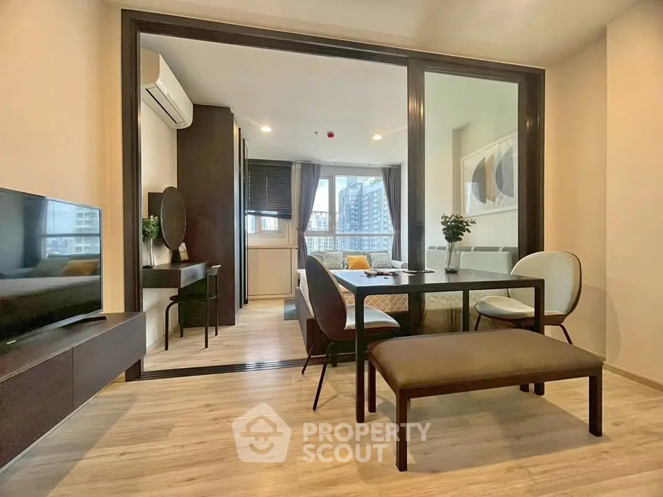 Modern living room with dining area and city view, featuring sleek furniture and large windows.