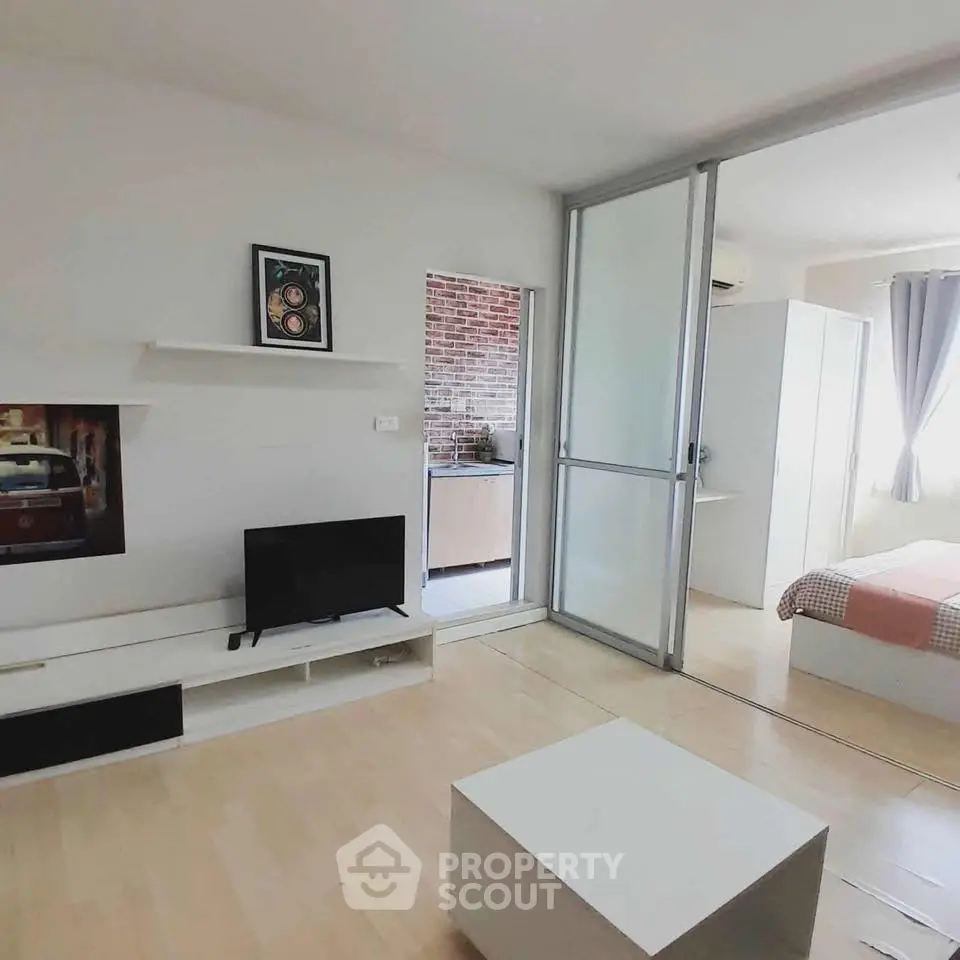 Modern studio apartment with open layout, featuring a cozy living area and bedroom separated by sliding glass doors.