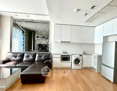 Modern open-plan living room with sleek kitchen and built-in appliances, featuring a stylish mirrored wall.