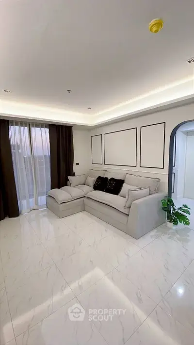 Elegant living room with modern decor, featuring a plush sectional sofa and large windows with sheer curtains.