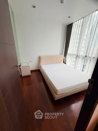 Modern bedroom with large window and wooden flooring in high-rise apartment.