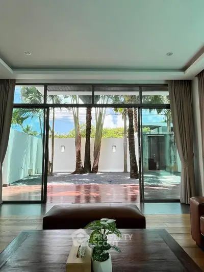 Luxurious living room with large glass doors opening to a tropical garden view, offering serene and elegant ambiance.