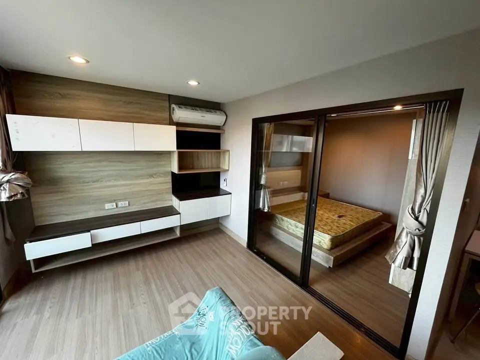Modern apartment interior with open living room and bedroom, featuring sleek wood flooring and stylish built-in storage.