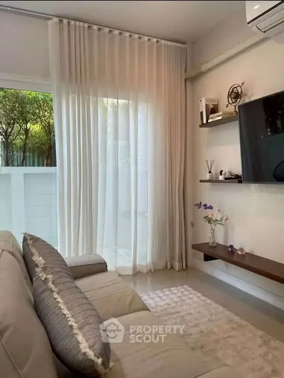 Chic modern living room with plush sofa, wall-mounted TV, and elegant sheer curtains opening to a serene garden view.