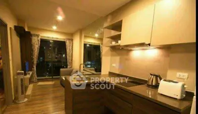 Modern kitchen with open layout and cozy living area, featuring sleek cabinetry and large windows.