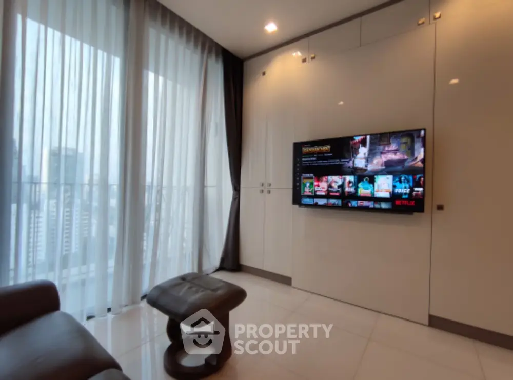 Modern living room with sleek design and city view, featuring wall-mounted TV and elegant furnishings.