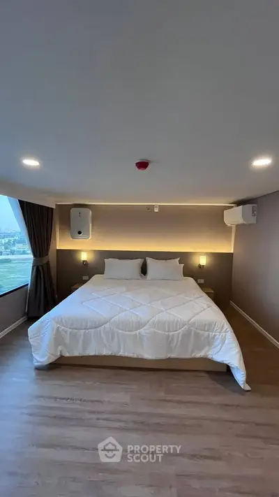 Modern bedroom with large window and stylish lighting, featuring a comfortable double bed and wooden flooring.