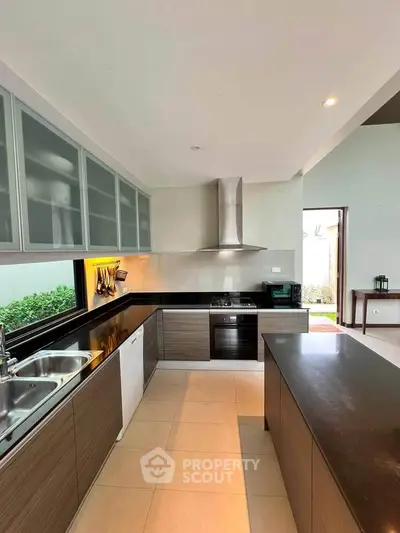 Modern kitchen with sleek cabinetry and island, featuring stainless steel appliances and garden view.
