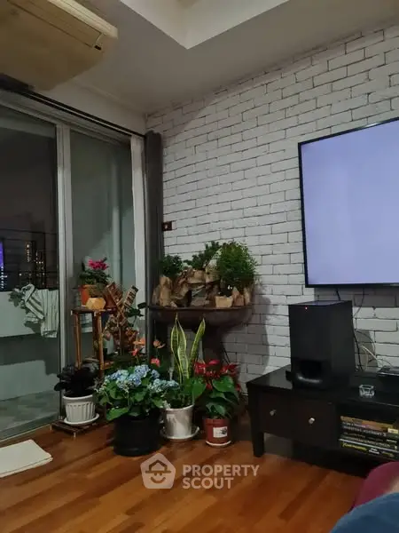 Charming living room with indoor plants and modern decor, featuring a wall-mounted TV and sliding glass doors to balcony.
