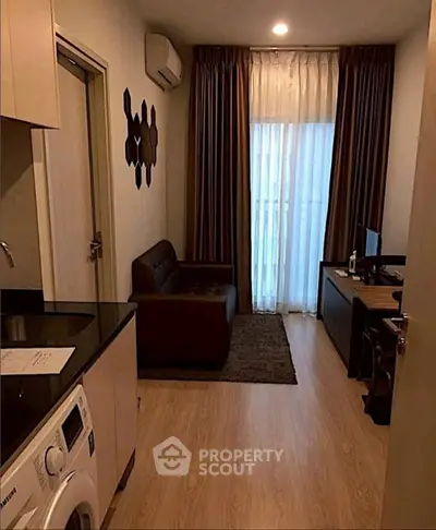 Cozy living room with modern decor and natural light, featuring a compact kitchen and stylish furnishings.