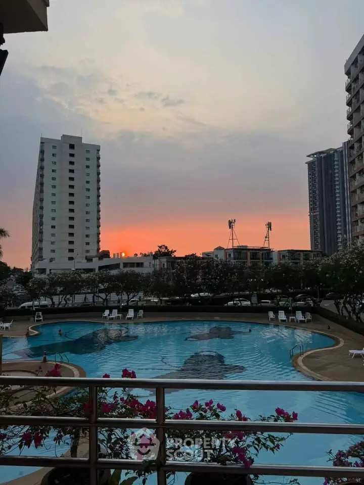 Stunning sunset view over a luxurious apartment pool with city skyline.