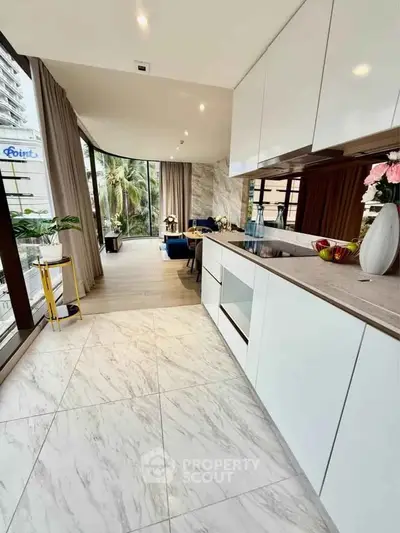 Modern open-layout kitchen with sleek cabinets and spacious living area, featuring large windows and elegant decor.