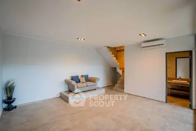 Spacious modern living room with minimalist design and cozy seating area, featuring neutral tones and elegant lighting.