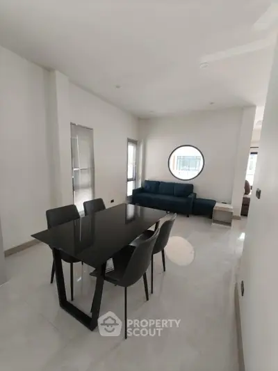 Modern living room with sleek black dining table and stylish round window, perfect for contemporary living.