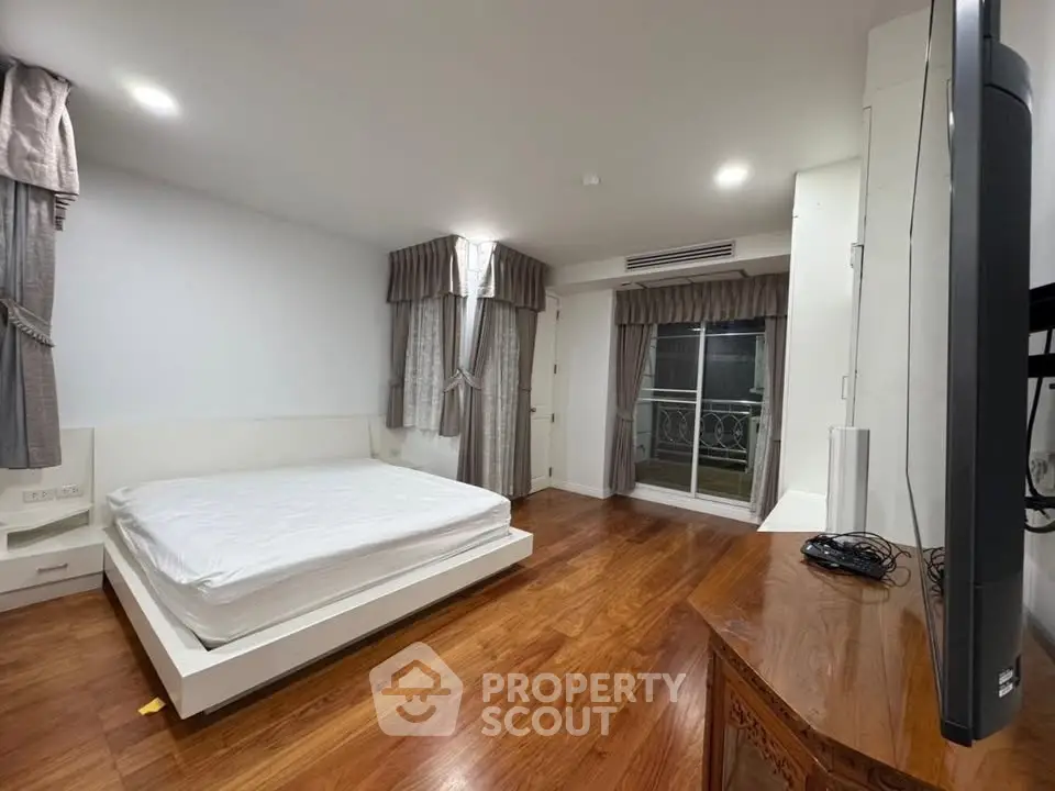 Spacious bedroom with hardwood floors and elegant drapery in modern apartment.