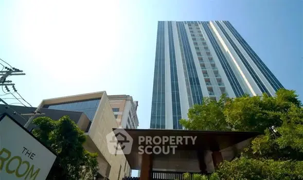 Modern high-rise building with sleek glass facade and lush greenery at entrance.