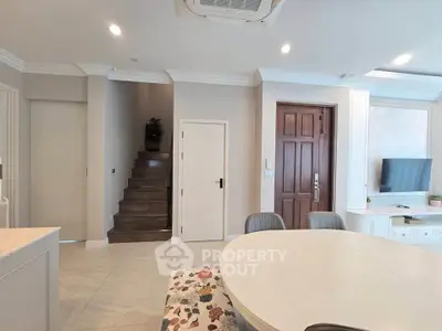 Modern living room with elegant dining area and staircase, featuring neutral tones and stylish decor.