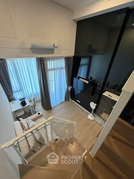 Modern loft apartment with high ceilings and large windows, featuring a cozy living area and stylish staircase.