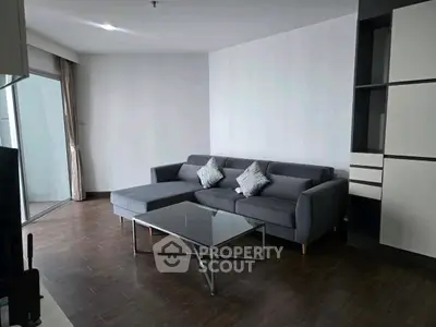 Modern living room with sleek gray sofa and glass coffee table, featuring built-in shelving and balcony access.