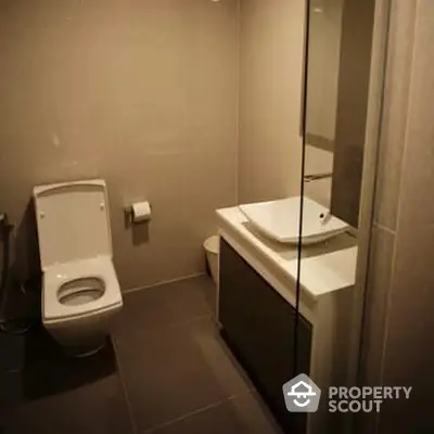 Compact modern bathroom with sleek fixtures, including a wall-mounted toilet and a stylish vanity sink, complemented by neutral-toned tiles.