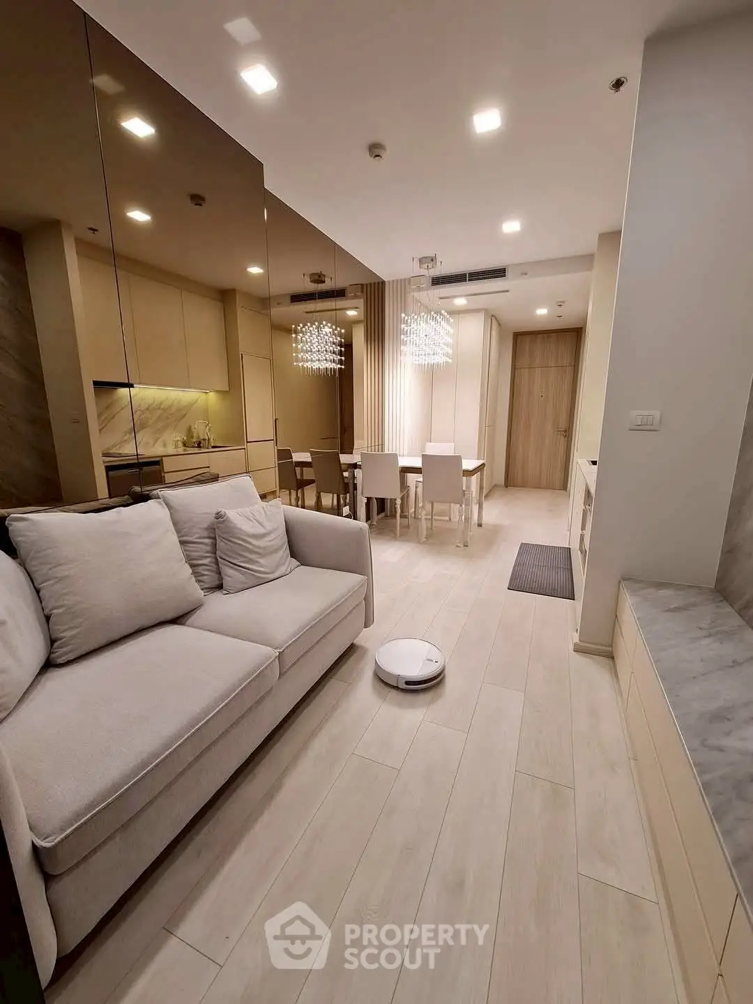 Modern open-plan living room with sleek kitchen and dining area, featuring elegant lighting and neutral decor.