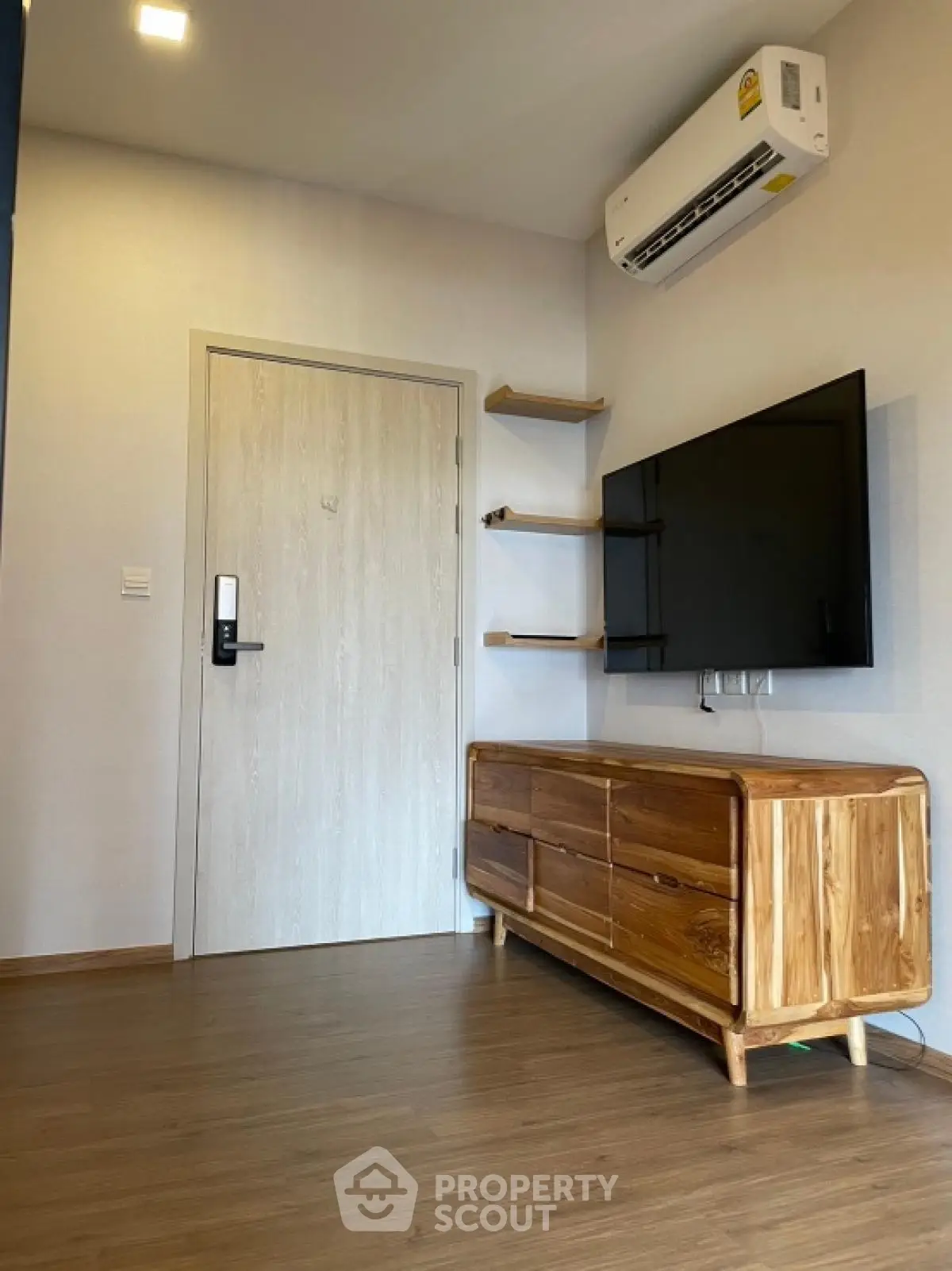 Modern living room with wooden flooring, wall-mounted TV, and sleek air conditioning unit.