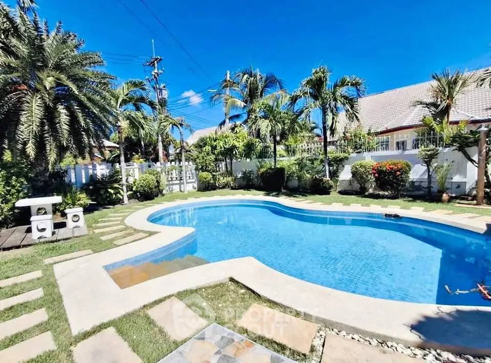 Stunning backyard pool with lush tropical landscaping and clear blue sky.