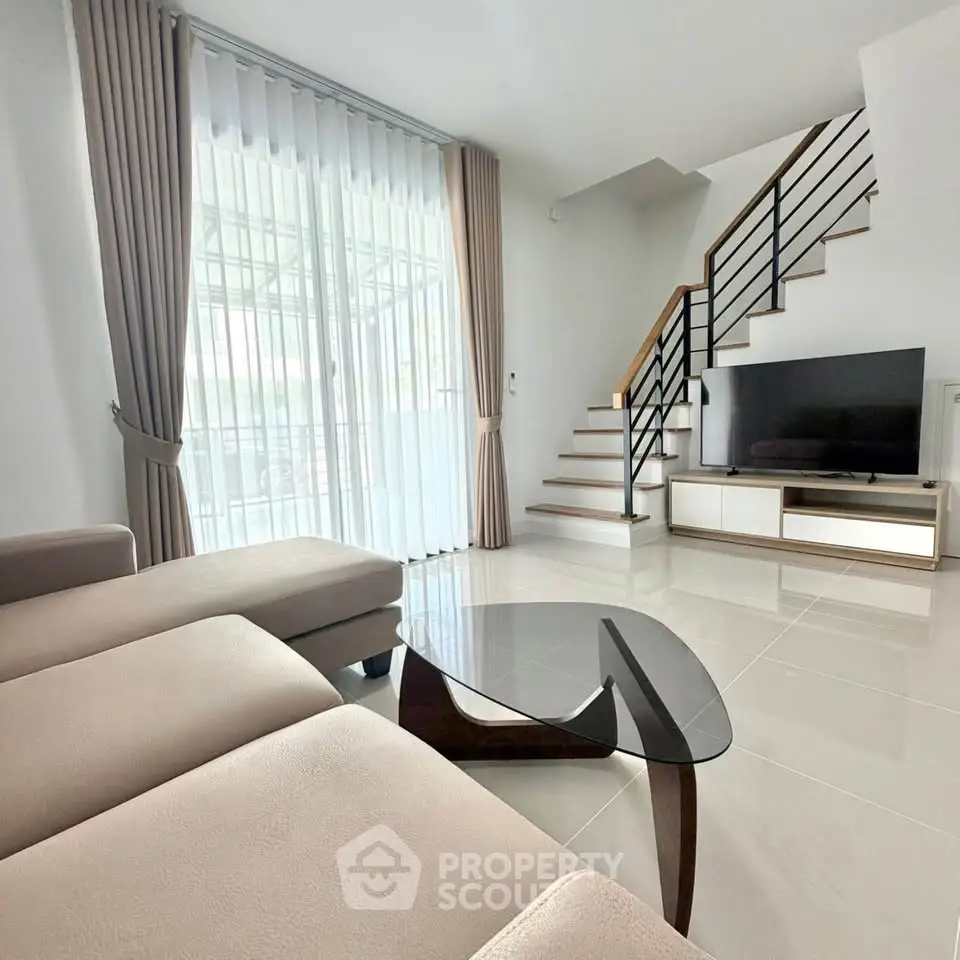 Modern living room with sleek staircase and large windows, featuring a stylish sofa and glass coffee table.