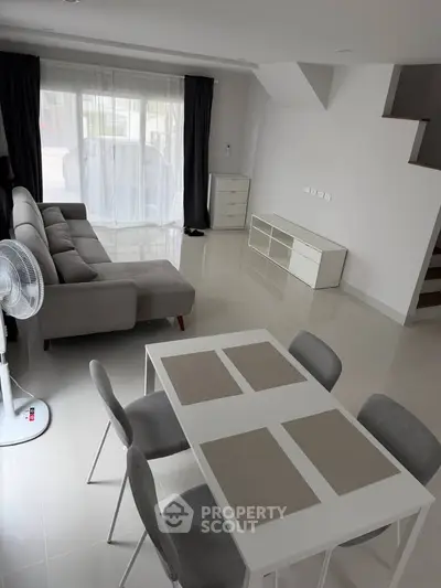 Modern living room with sleek furniture and dining area in a bright, open space.