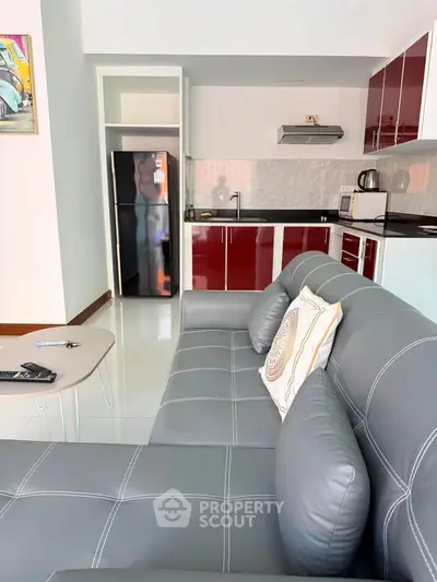 Modern open-layout kitchen and living room with sleek red cabinets and stylish gray sofa.