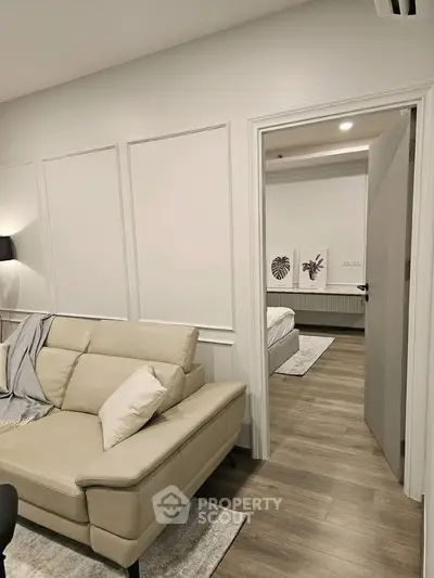 Modern living room with beige leather sofa and view into a cozy bedroom, featuring elegant decor and wooden flooring.