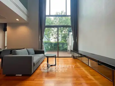 Spacious living room with high ceilings and large windows opening to a balcony with a view.