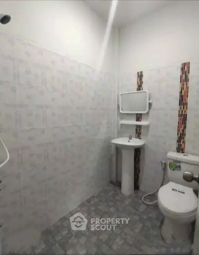 Compact bathroom with tiled walls and floor, featuring a toilet, sink, and mirror.