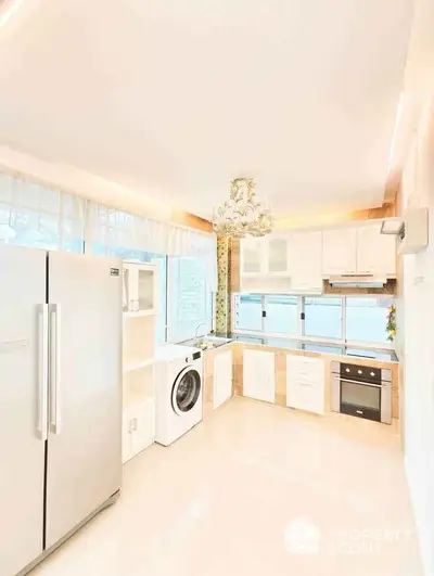 Bright modern kitchen with large fridge, washing machine, and elegant chandelier