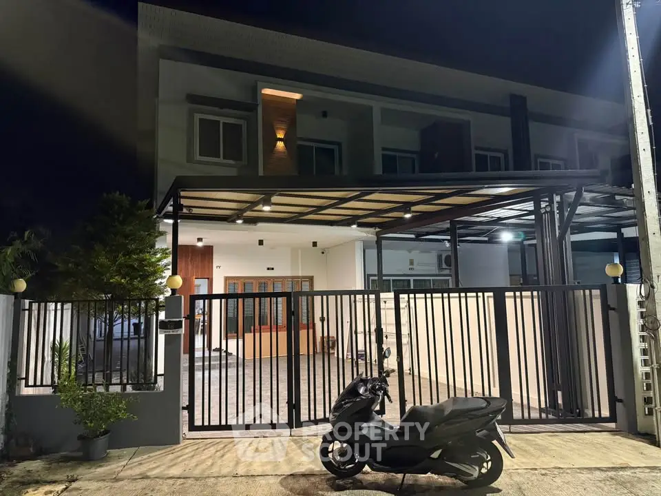 Modern two-story house with gated entrance and covered parking at night